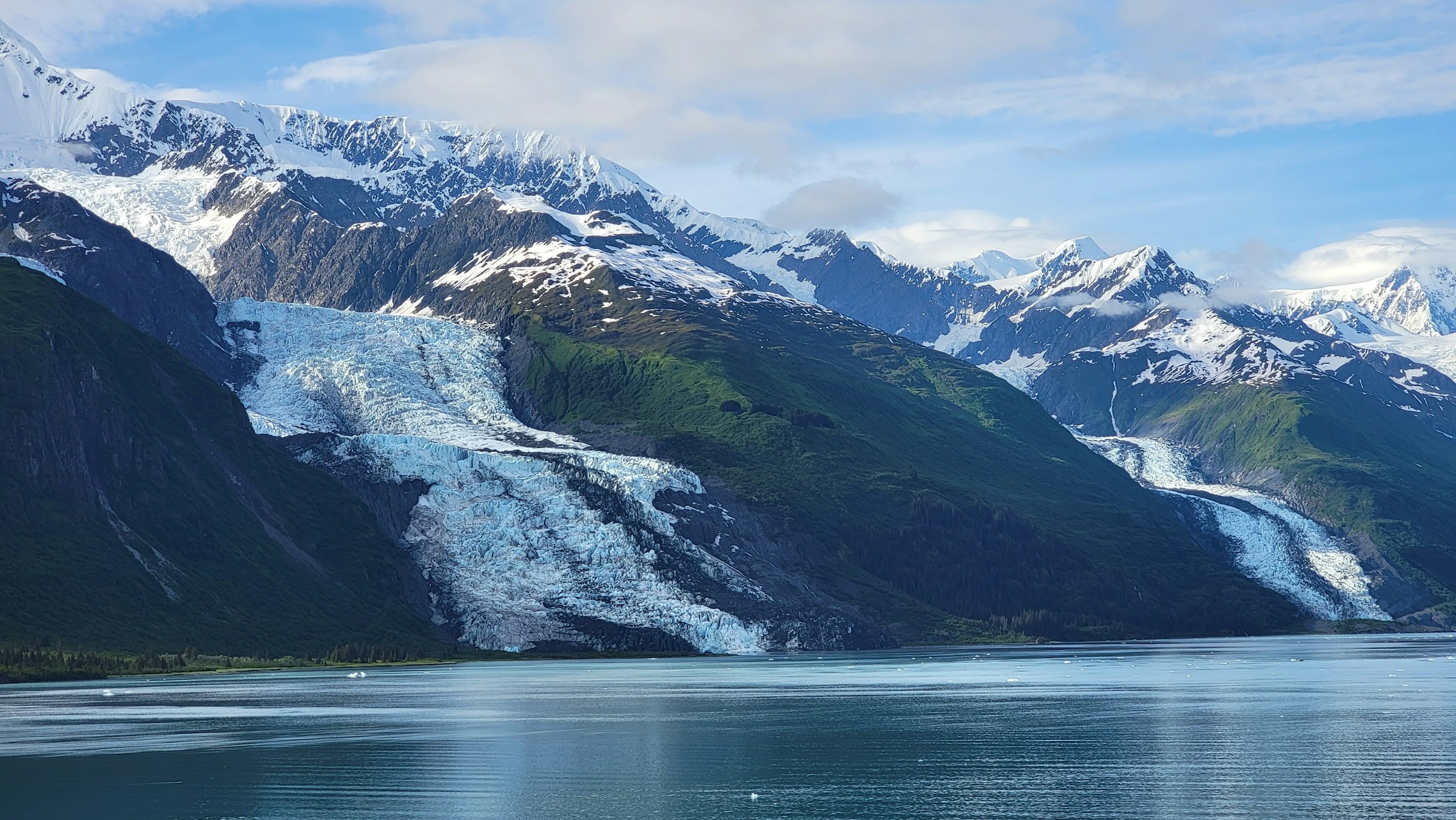 Two glaciers coming down snowy mountains to the edge of a calm Alaskan bay