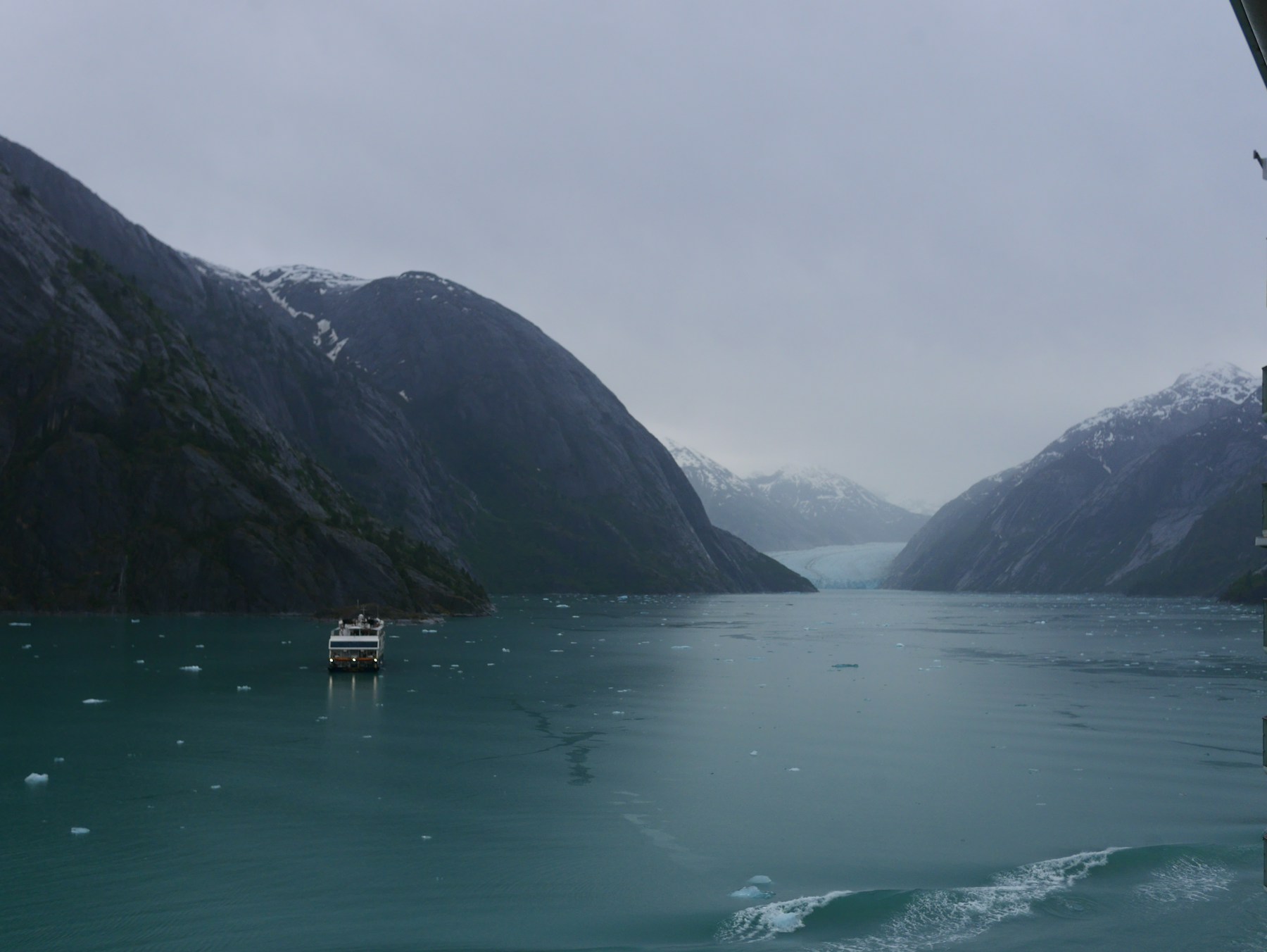 A ship in a narrow Alaskan fjord with ice floating in the water
